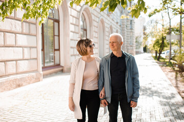 Senior happy couple of stylish man and woman 60-65 year old walking together on streets at city outdoors. Wellness lifestyle.