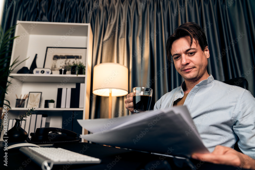 Poster sales manager working on pc and compare with business graph report while drinking coffee at night ti