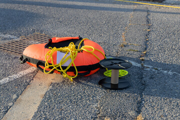 Bright orange life buoy with yellow rope and spool resting on a textured surface, symbolizing safety and summer water activities