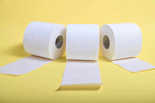 Three rolls of soft white toilet paper sit against a bright yellow background, highlighting hygiene