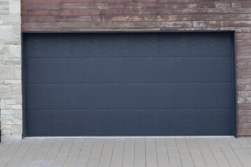 A large black residential hinged panel door in a brown cedar exterior wall with light grey brick....