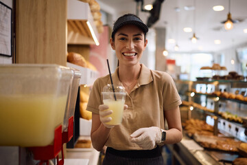 Happy female baker serving fresh lemonade and looking at camera.