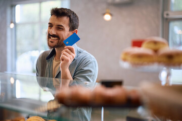 Happy man paying with credit card in bakery.