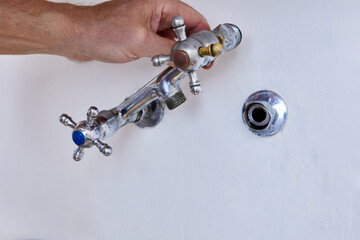 Removing old wall mounted kitchen faucet with two cross handles from hidden pipe in concrete wall,...