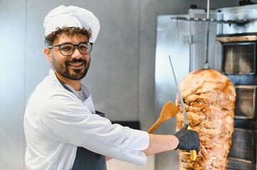 Chef slicing kebab meat from vertical rotisserie in restaurant kitchen