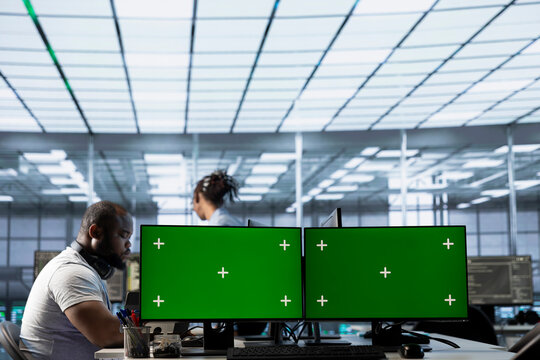 Data center employees using isolated screen multi monitor PC setup to write disaster recovery plans ensuring minimal downtime. Server farm engineers use chroma key computer to monitor performance
