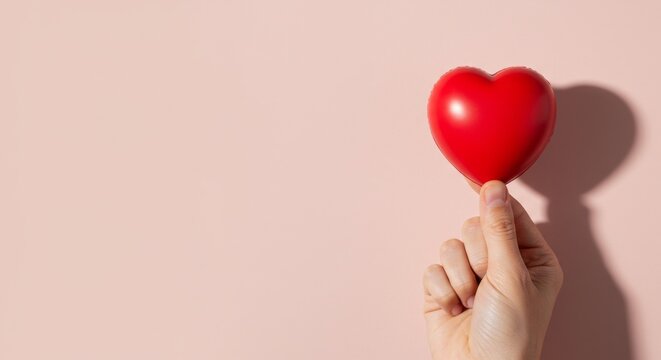 Hand holding red heart symbol on soft pink background