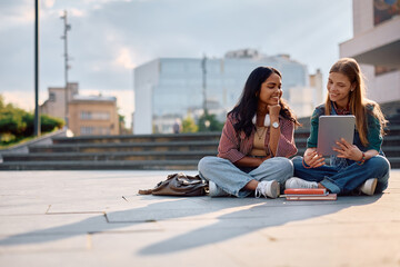 Happy female students e-learning on touchpad at university campus.