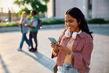 Happy Indian female student using smart phone at university campus.
