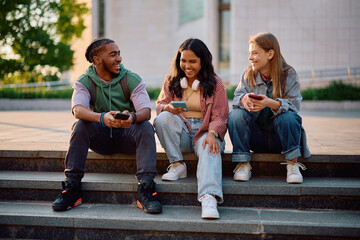 Happy college friends having fun while using their cell phone at campus.