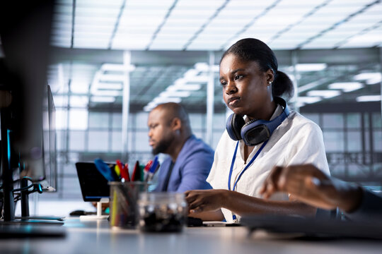 African american engineer next to coworkers in server farm checking recovery plan, monitoring data center energy consumption. Woman in server hub doing routine disk checks