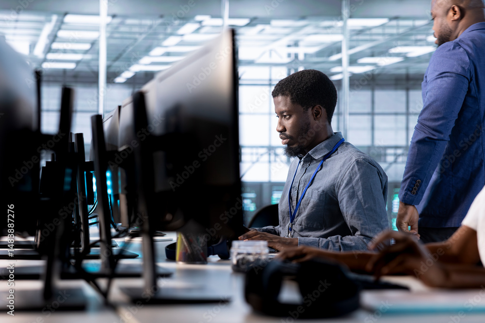 Poster engineer next to coworkers in server farm checking recovery plan, monitoring data center energy cons