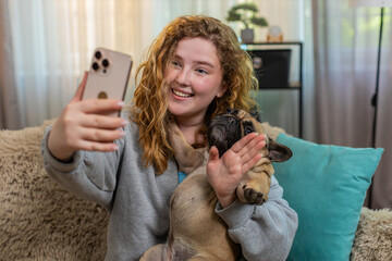 Young Caucasian blogger woman waves hand during video call conversation on home sofa, smiling and...
