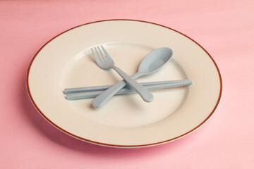 Empty plate with plastic spoon, fork and chopsticks on pink background.