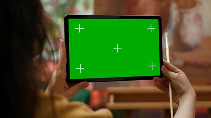 Painter holding a device with isolated mockup screen in her art studio, looking at her finished masterpiece with oil paints on canvas. Beautiful rustic artwork for a fine art gallery. Camera A.