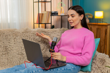 Young woman at home recording podcast speaking into microphone with serious, focused expression....