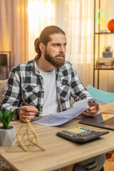 Young serious man checks papers at home table reading fine print new agreement with deep concern...
