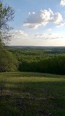 Obraz premium Serene Landscape, Rolling Hills and Lush Green Forest Under a Cloudy Sky