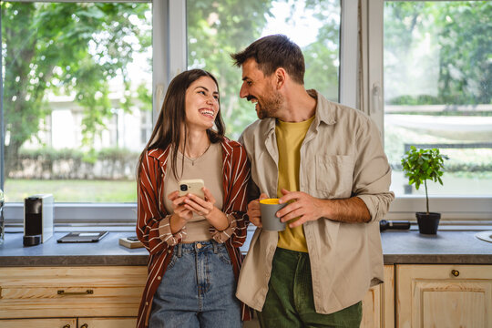 happy couple stand in the kitchen and use mobile phone together