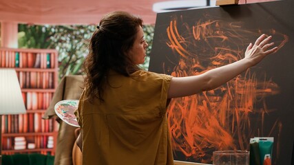 Painter works with finger painting technique on her latest artwork piece, contemporary art studio buzzes with creativity. Artist uses vibrant colors and for a modern paintwork design. Camera A.