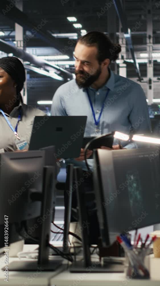 Poster vertical video smiling engineering team in server room reviewing infrastructure diagnostics on devic