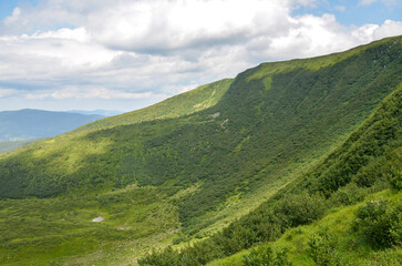 Lush green hill slope overlooking vast mountain range beneath blue sky with clouds. Nature's...