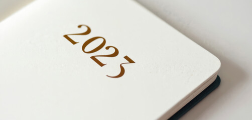 Minimalist 2023 planner with gold embossed lettering on white paper. Useful for organizing schedule daily plans. Ideal for business notes, reminders. Notebook with blank pages for daily usage.