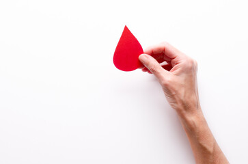 A female hand holding a paper drop of blood on white background and copy space.