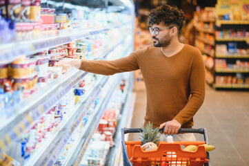 Arab man choosing yogurt in supermarket refrigerator while shopping groceries