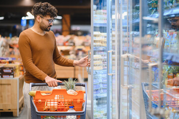 Arab man opening refrigerator in supermarket while shopping for groceries
