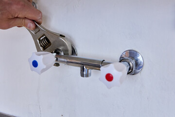 Tightening of wall-mounted tap connection is performed by plumber using adjustable wrench with...