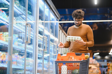 Arab man choosing eggs in refrigerated section of supermarket