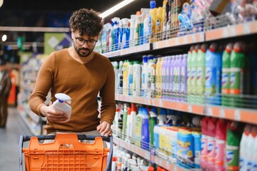 Arab man choosing cleaning product in supermarket while shopping for groceries