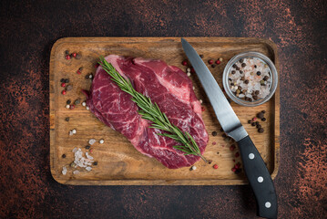Raw Rib Eye steak with spices on a wooden board on a dark background. View from above.