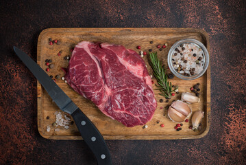 Raw Rib Eye steak with spices on a wooden board on a dark background. View from above.