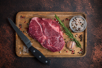Raw Rib Eye steak with spices on a wooden board on a dark background. View from above.