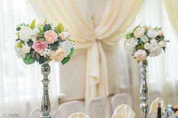 The central decoration of white and pink flowers stands on a silver stand on a decorated table and is part of a wedding or formal event, banquet hall