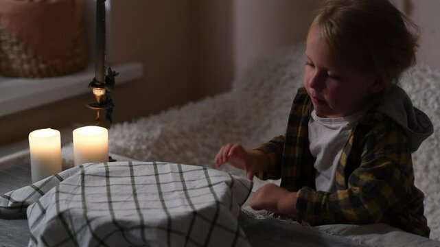 Girl sits by covered dough bowl at night, curiously peeking under the towel.