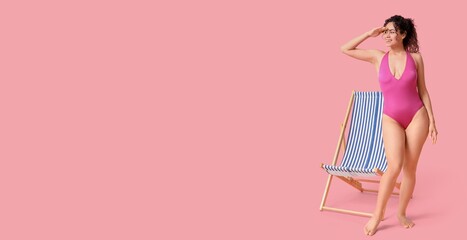 Beautiful young African-American woman in swimsuit near deck chair on pink background with space for text