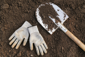 Digging up dry soil in garden. Soil ground texture background with shovel and gloves close up top...