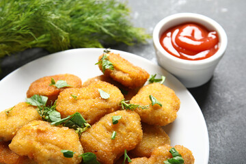 Plate with tasty nuggets, ketchup and herbs on black table