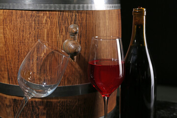 Wooden barrel with bottle and glasses of wine on dark background, closeup