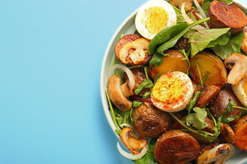 Plate of tasty potato salad with eggs and mushrooms on light blue background, closeup