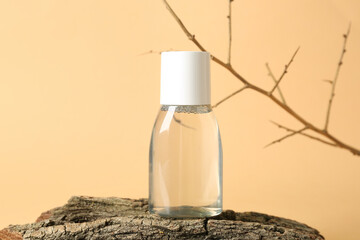 Bottle of micellar water with tree branch and bark on beige background, closeup