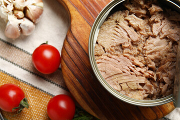 Board with opened tin can of tuna, tomatoes and garlic on napkin, closeup