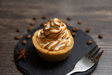 Toasted Meringue Tartlet with Coffee Beans. Mini tart topped with beautifully toasted meringue, surrounded by scattered coffee beans and star anise on a rustic background.