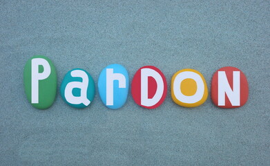 Pardon, the action of forgiving or being forgiven for an error or offence, creative word composed with multi colored hand painted stone letters over green sand