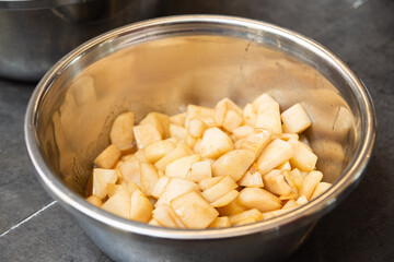 Cinnamon spiced chopped apples in metal bowl. A bowl of freshly chopped apples coated with cinnamon and sugar, ready for baking or dessert preparation in a kitchen setting.