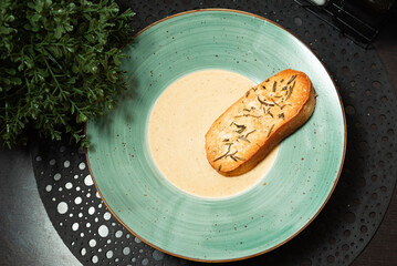 Creamy Soup with Herb Crouton in Green Bowl. Gourmet creamy soup served in a rustic green bowl, topped with a toasted herb crouton for a cozy appetizer presentation.