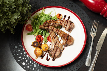 Gourmet Lamb Chops with Salad and Balsamic Glaze. Elegant plate of grilled lamb chops served with arugula, cherry tomatoes, roasted potatoes, and balsamic glaze for fine dining menus. © obsidianium